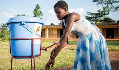African lady washing her hands from a raised blue bucket with a spout