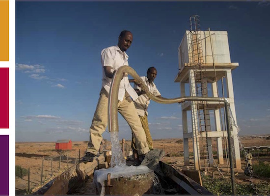 Two African men holding a large water hose connected to a water tower